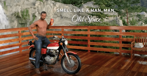 Shirtless sits on motorcycle while holding Old Spice can. 